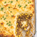 Bird’s-eye view of vintage Chinese pie casserole with a scoop missing, showing layers of mashed potatoes, sweet corn, and ground beef with a serving spoon in the dish.