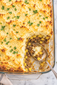 Bird’s-eye view of vintage Chinese pie casserole with a scoop missing, showing layers of mashed potatoes, sweet corn, and ground beef with a serving spoon in the dish.