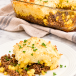 Vintage Chinese pie casserole with layers of ground beef, sweet corn, and mashed potatoes served on a white plate beside a glass baking dish.