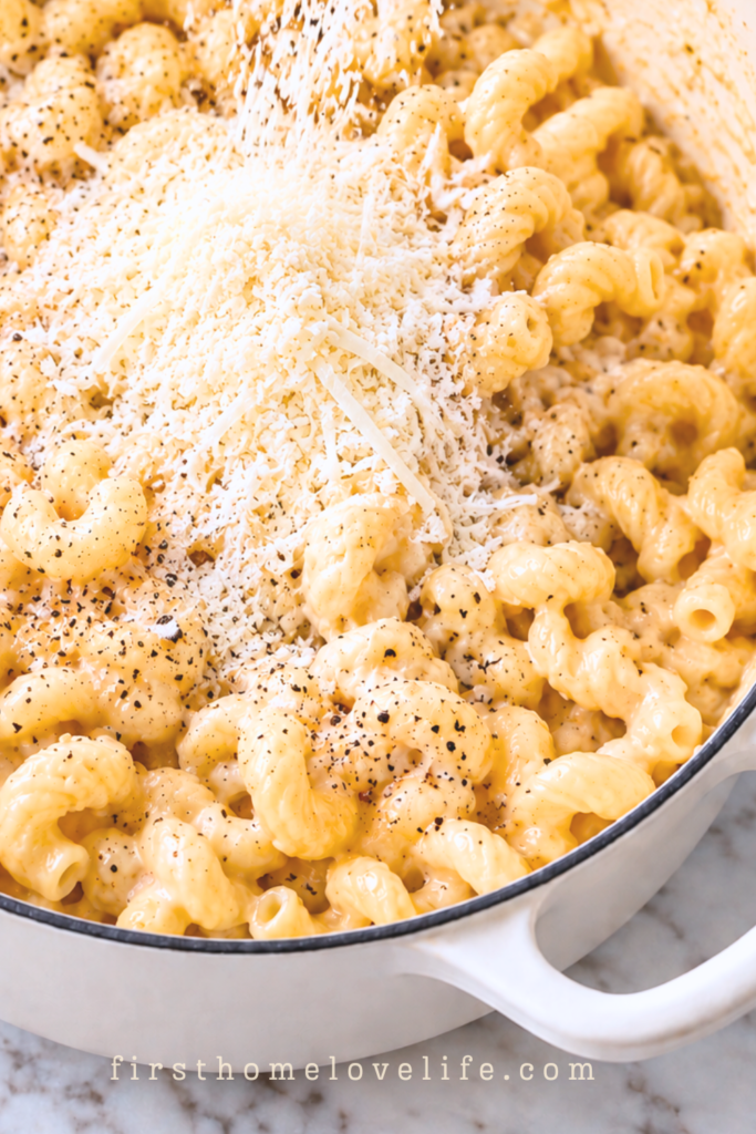 Freshly grated Pecorino Romano and Parmesan being added to cooked cavatappi pasta in a white pot for one pot cacio e pepe mac and cheese.