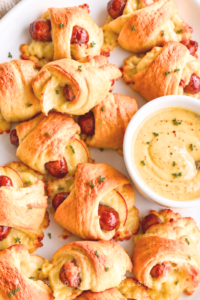 Apple Gouda pigs in a blanket with golden crescent rolls and a light thyme garnish on a white platter beside maple mustard dip.