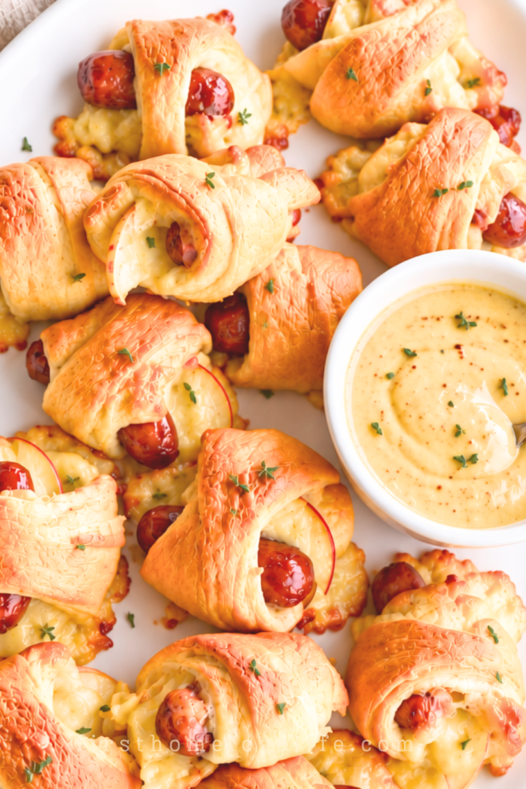 Apple Gouda pigs in a blanket with golden crescent rolls and a light thyme garnish on a white platter beside maple mustard dip.