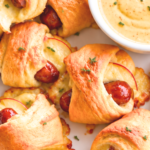 Apple Gouda pigs in a blanket with golden crescent rolls and a light thyme garnish on a white platter beside maple mustard dip.