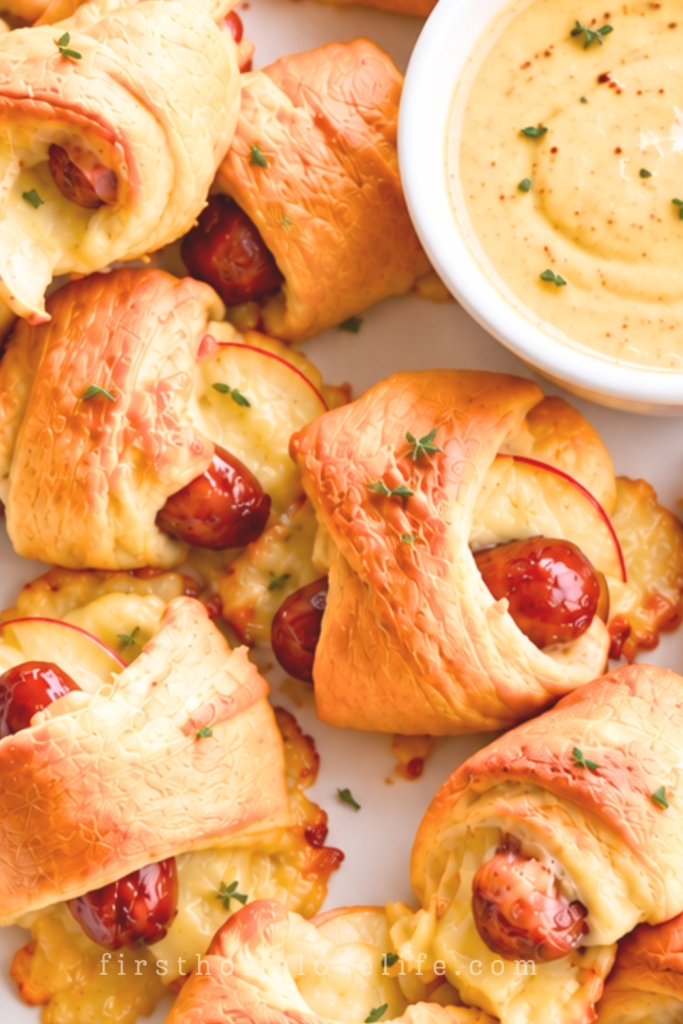 Apple Gouda pigs in a blanket with golden crescent rolls and a light thyme garnish on a white platter beside maple mustard dip.