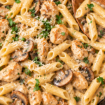 Overhead view of copycat Pasta Da Vinci with chicken, penne, and mushrooms in creamy Madeira sauce in a cast iron skillet with a wooden spoon.