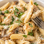 Copycat Cheesecake Factory Pasta Da Vinci with penne, chicken, mushrooms, and creamy Madeira sauce in a white bowl with a silver fork.