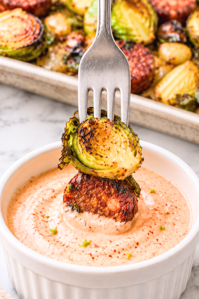 A fork holding a roasted Brussels sprout and chorizo slice vertically in smoky lime dipping sauce.