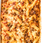 Overhead view of sausage and pumpkin baked ziti with golden melted cheese and ricotta in a white casserole dish.