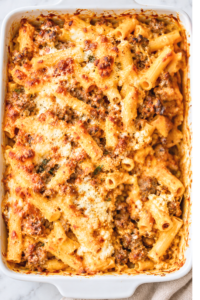 Overhead view of sausage and pumpkin baked ziti with golden melted cheese and ricotta in a white casserole dish.