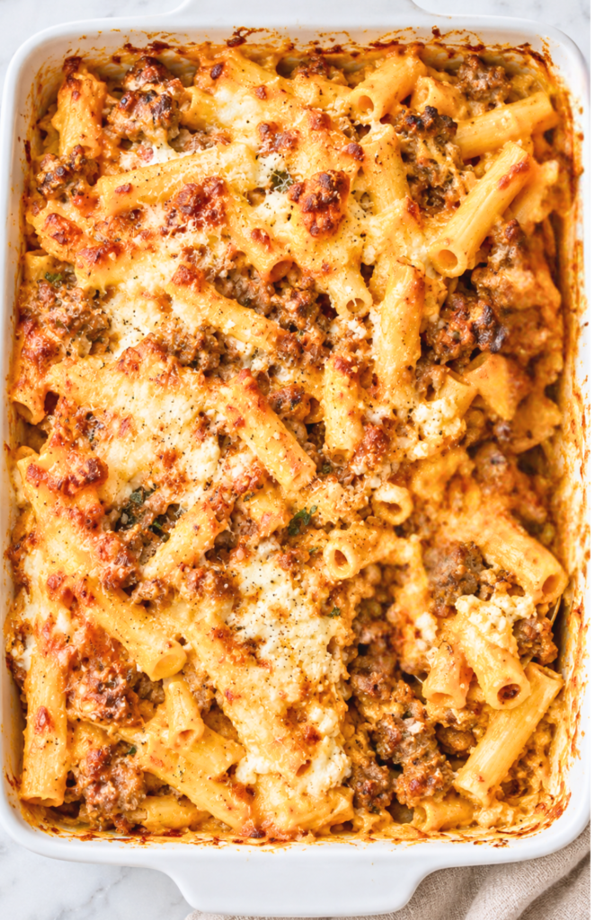 Overhead view of sausage and pumpkin baked ziti with golden melted cheese and ricotta in a white casserole dish.