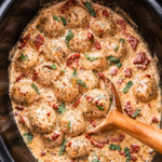 Creamy Crockpot Marry Me Chicken Meatballs with sun-dried tomatoes, parmesan, and fresh basil in a black slow cooker.