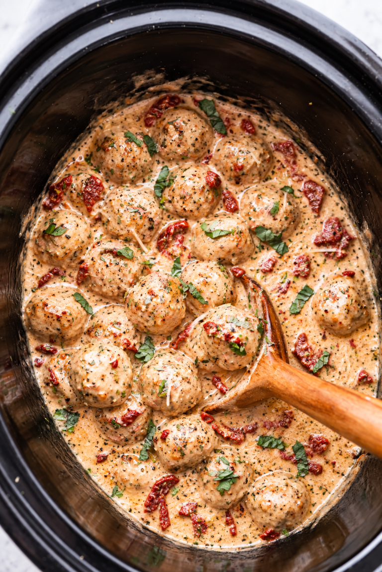 Creamy Crockpot Marry Me Chicken Meatballs with sun-dried tomatoes, parmesan, and fresh basil in a black slow cooker.