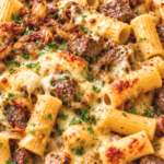 French onion beef pasta with rigatoni, seared steak, caramelized onions, and golden melted Gruyère in a white skillet.