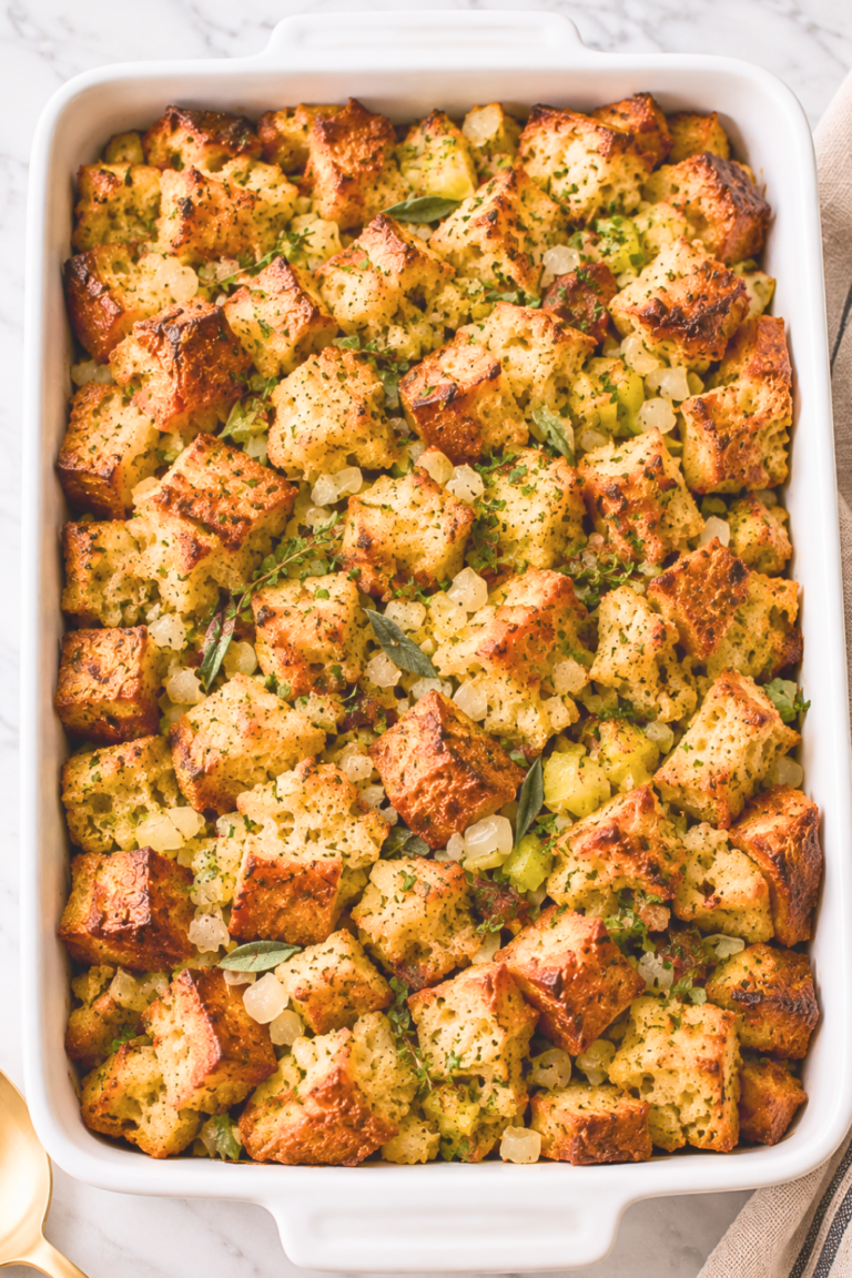 Overhead view of homemade sourdough stuffing with golden toasted bread cubes, celery, onions, and fresh herbs in a white casserole dish.