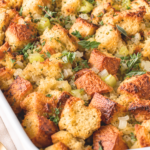Homemade sourdough stuffing with golden crispy bread cubes, fresh herbs, celery, and onions baked in a white casserole dish.