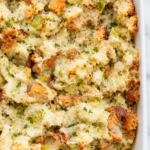 Pennsylvania Dutch potato filling with golden bread pieces, creamy mashed potatoes, celery, and parsley in a white casserole dish on marble.