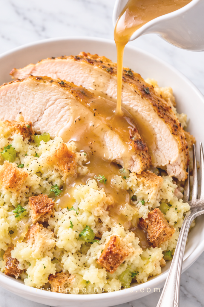 Gravy pouring over sliced turkey and Pennsylvania Dutch potato filling in a white bowl with a silver fork tucked beside it.