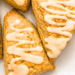Close-up of golden triangular pumpkin spice scones topped with thick pumpkin latte glaze on a white platter.