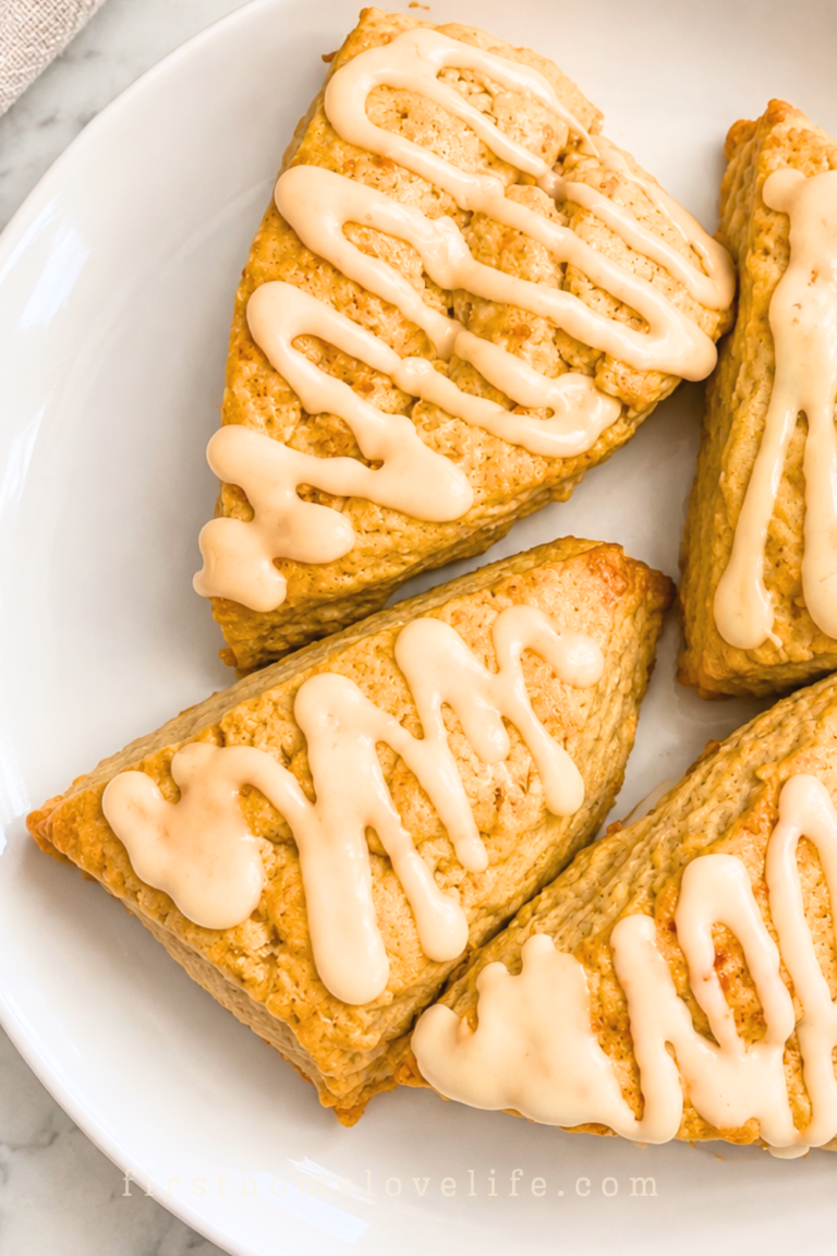 Four golden pumpkin spice scones drizzled with pumpkin latte glaze on a white platter over a marble countertop.
