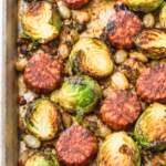 Close-up of roasted Brussels sprout halves and browned chorizo slices on a sheet pan.
