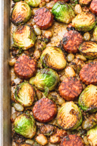 Close-up of roasted Brussels sprout halves and browned chorizo slices on a sheet pan.