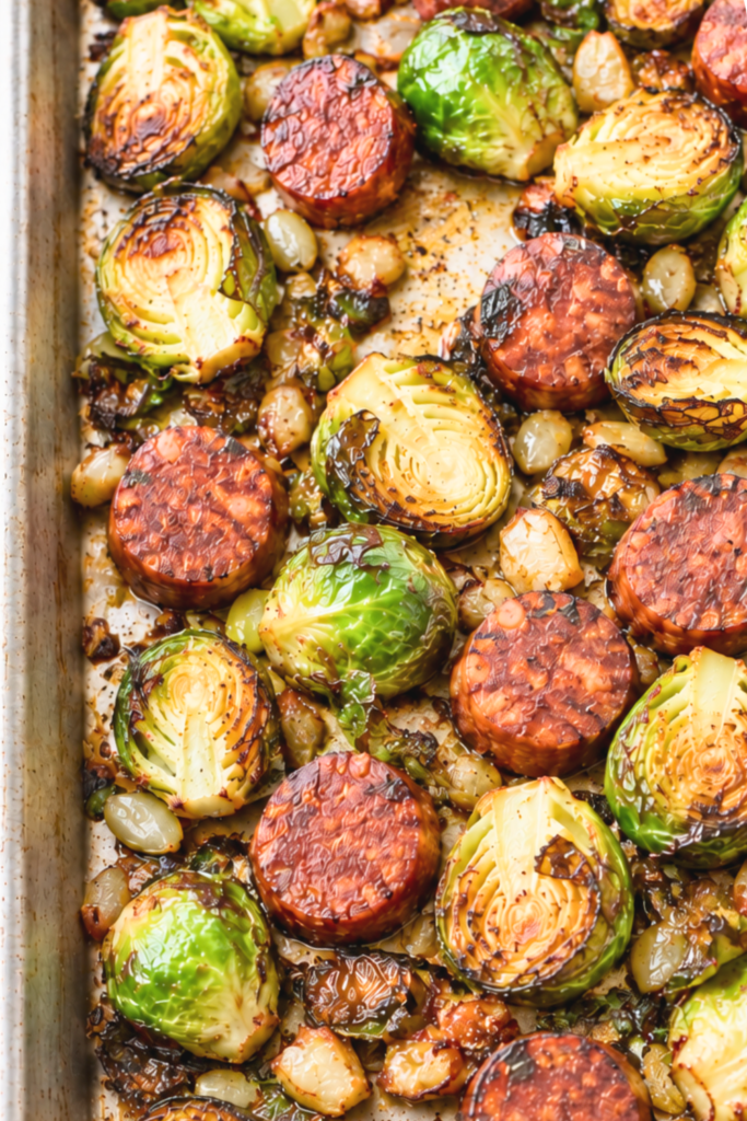 Close-up of roasted Brussels sprout halves and browned chorizo slices on a sheet pan.