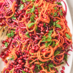 Close-up of roasted sweet potato spiral salad with red beets, pomegranate seeds, fresh mint, parsley, and homemade pomegranate dressing.