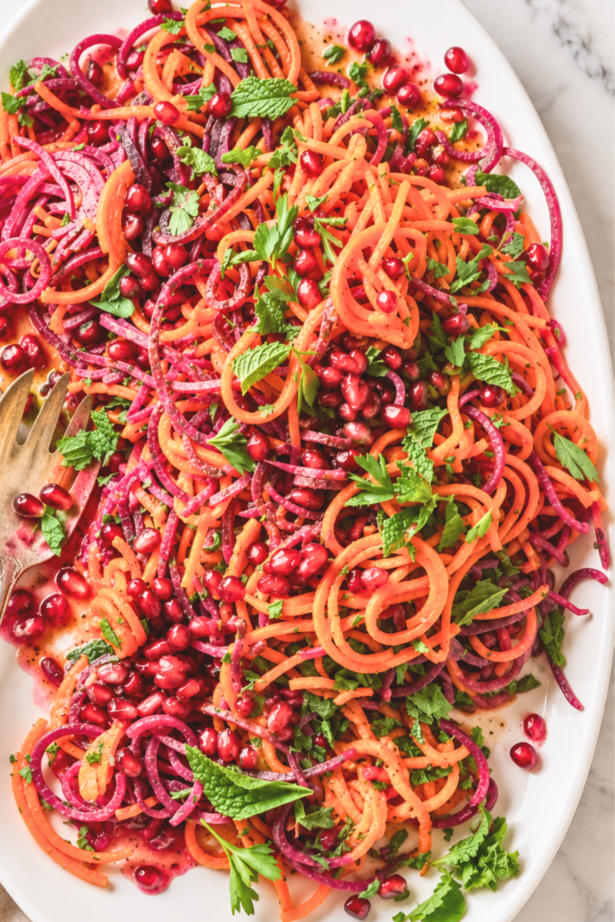 Close-up of roasted sweet potato spiral salad with red beets, pomegranate seeds, fresh mint, parsley, and homemade pomegranate dressing.