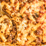 Sausage and pumpkin baked ziti with melted mozzarella and ricotta in a white casserole dish with a gold serving spoon.