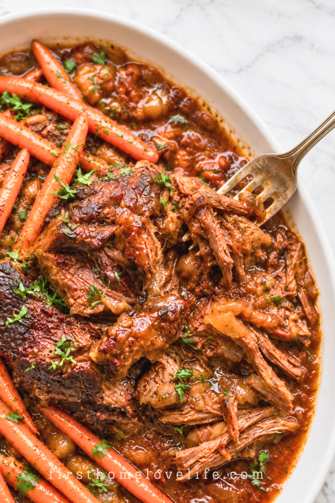 Slow cooker chuck roast with long carrots and thick pomegranate apple cider gravy on a white platter.